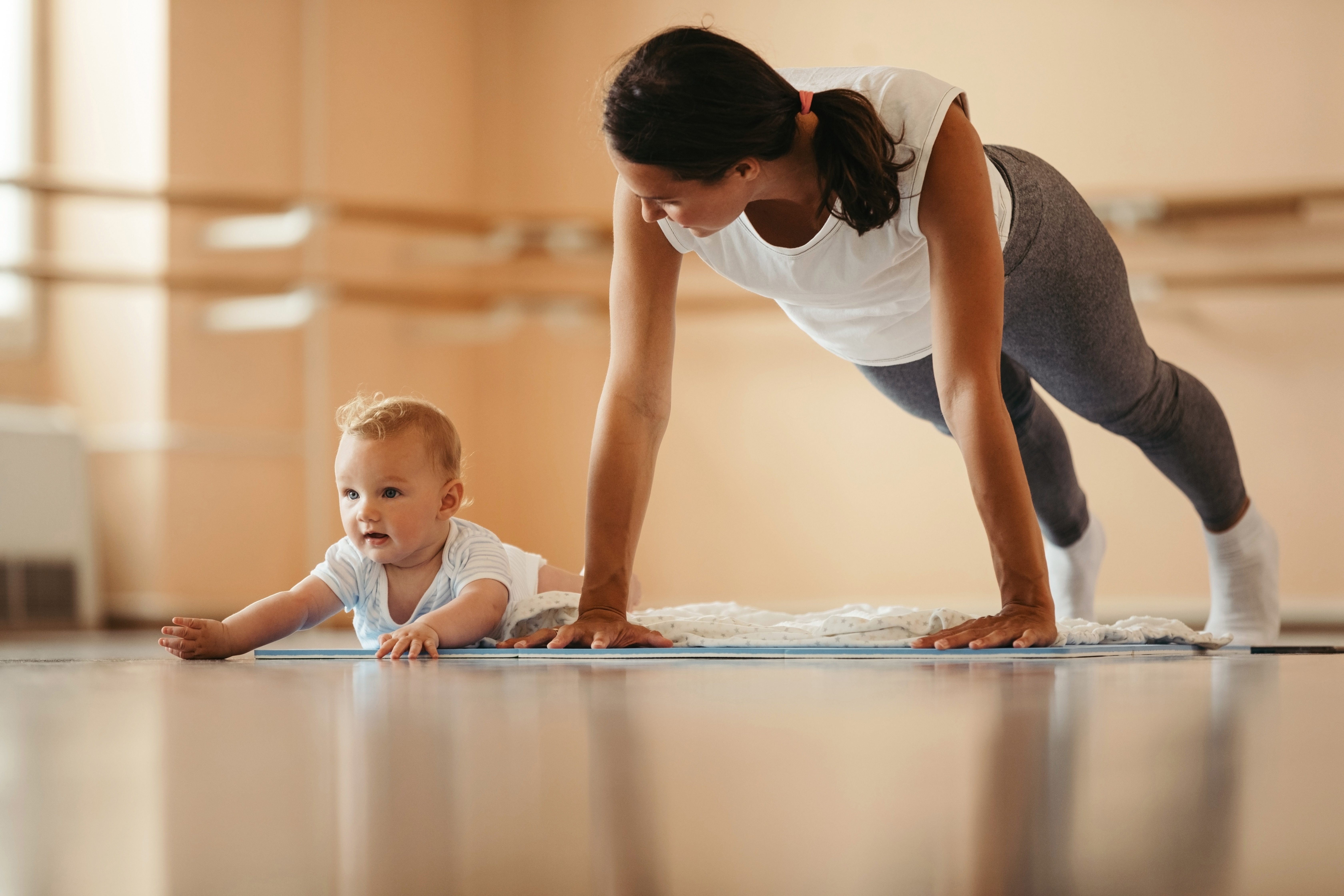 Athletic mother doing push-ups while practicing with her baby in health club. 