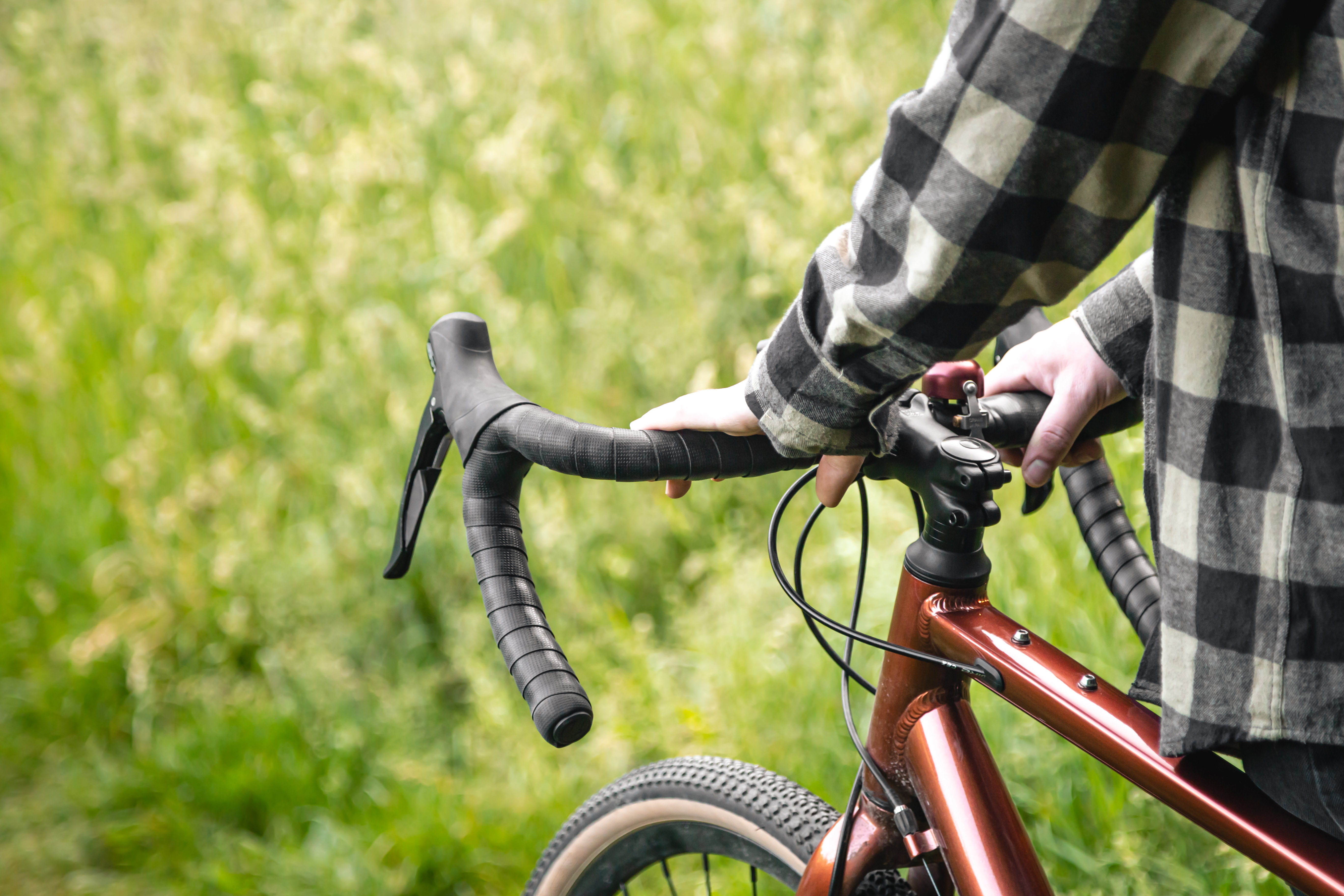 A man holds a bicycle handlebar and walks in the forest, close-up.